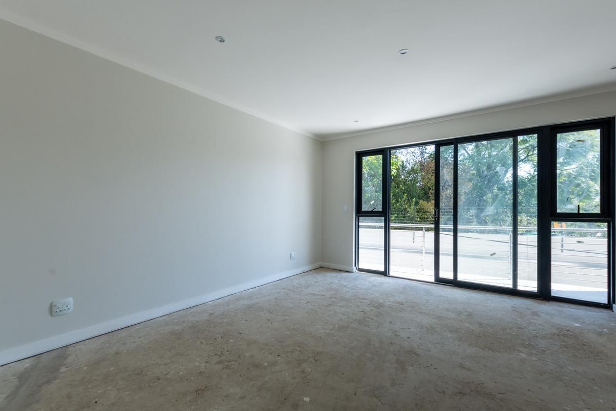 An empty bedroom featuring large black-framed sliding glass doors that open onto a balcony, providing natural light and outdoor access.