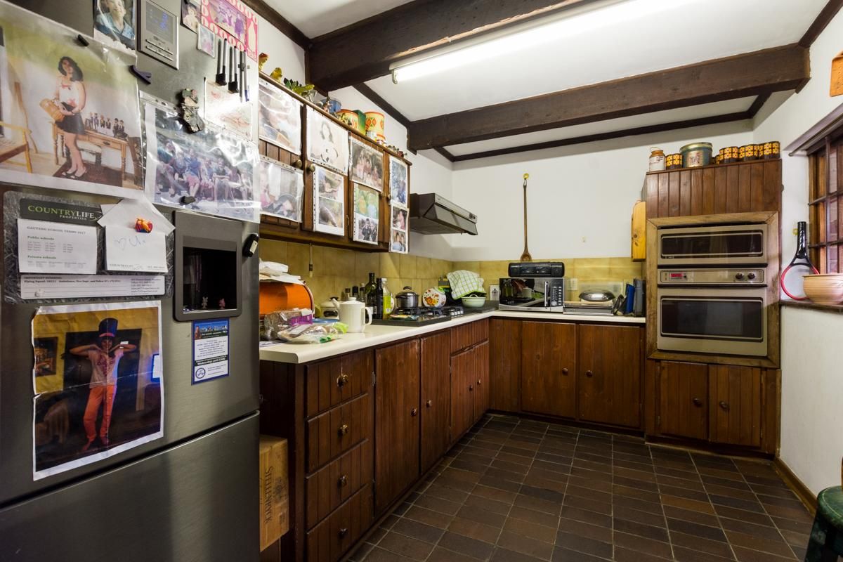 A dated kitchen featuring dark wood cabinetry, built-in oven and microwave, tiled countertops, and exposed ceiling beams.