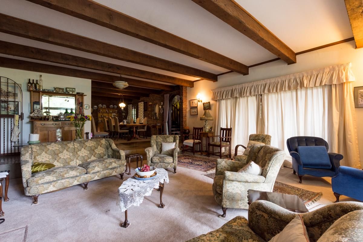 Spacious living area featuring exposed timber ceiling beams, brick accents, and large windows with floor-to-ceiling curtains, creating a warm and traditional atmosphere.