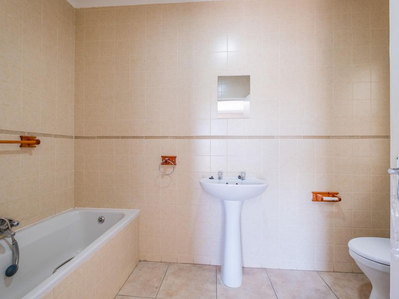 A functional bathroom featuring a pedestal basin, built-in bathtub, and wall-mounted toilet, finished with neutral ceramic wall and floor tiles.