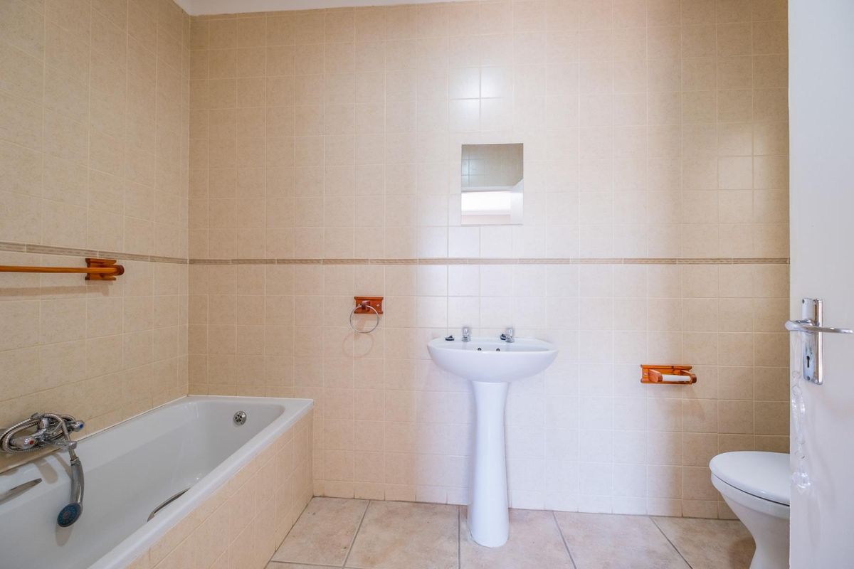 A functional bathroom featuring a pedestal basin, built-in bathtub, and wall-mounted toilet, finished with neutral ceramic wall and floor tiles.