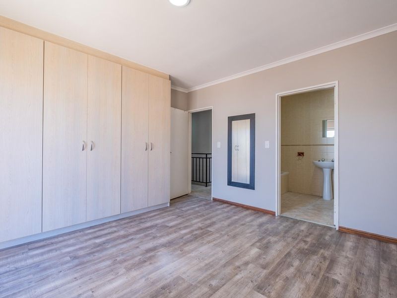 A spacious, empty bedroom featuring light wood-look laminate flooring, extensive built-in cupboards, and direct access to an en-suite bathroom.