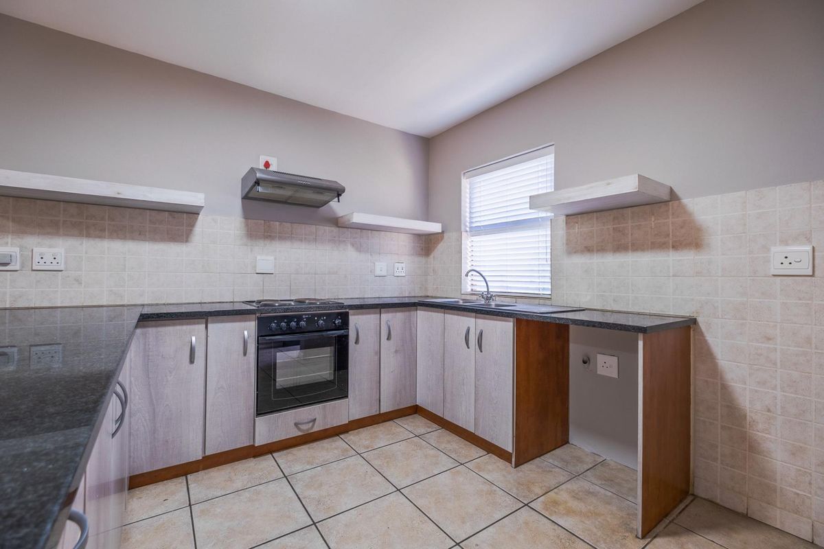 A functional kitchen featuring granite countertops, built-in oven with hob, extractor fan, and ample cabinetry, finished with tiled splashbacks and flooring.