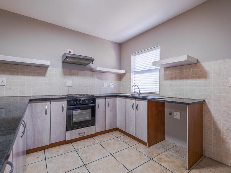 A functional kitchen featuring granite countertops, built-in oven with hob, extractor fan, and ample cabinetry, finished with tiled splashbacks and flooring.