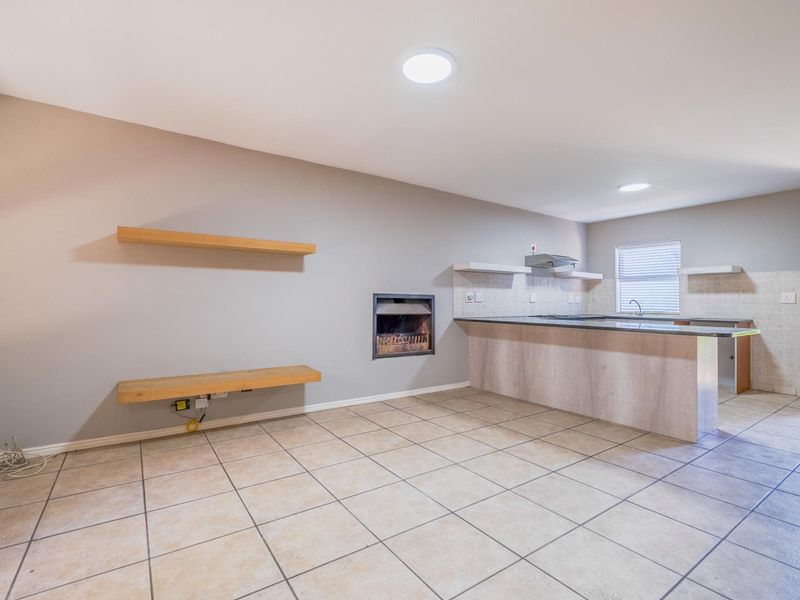 Open-plan living and kitchen area featuring a built-in fireplace, tiled flooring, and a kitchen island with integrated extractor fan and floating shelving.