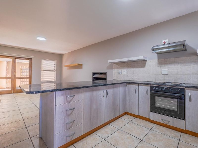 A functional kitchen featuring built-in cabinetry, granite countertops, a built-in oven with hob, and tiled flooring, leading to an adjacent living area.