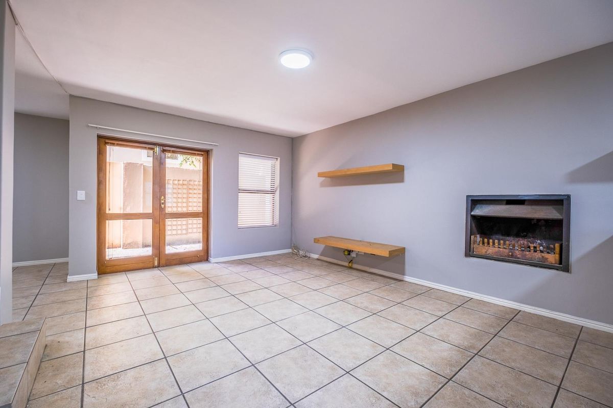 An empty living room featuring tiled flooring, a built-in fireplace, floating wooden shelves, and glass double doors leading to an outdoor area.