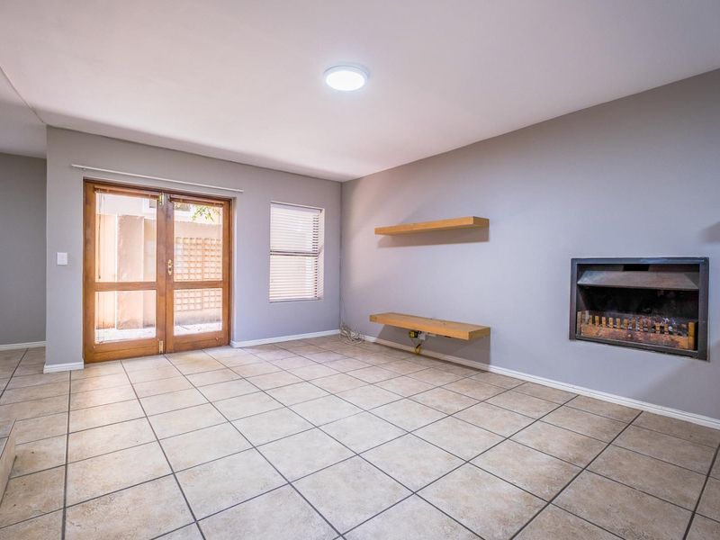 An empty living room featuring tiled flooring, a built-in fireplace, floating wooden shelves, and glass double doors leading to an outdoor area.