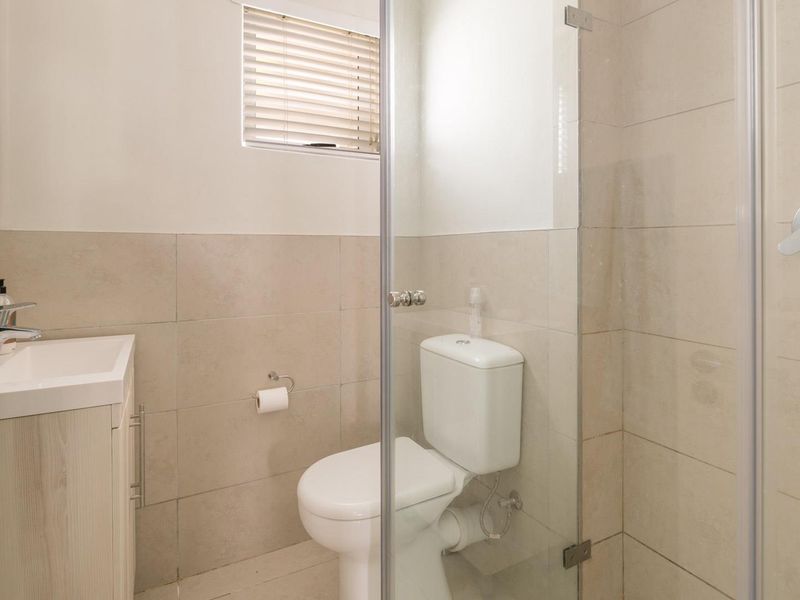A clean, modern bathroom featuring a vanity with basin, a toilet, and a glass-enclosed shower with neutral wall tiling.