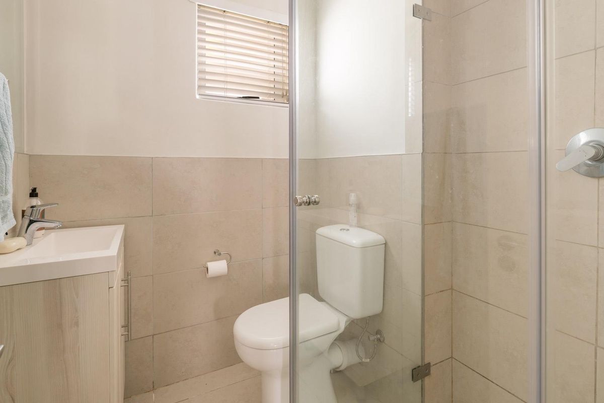 A clean, modern bathroom featuring a vanity with basin, a toilet, and a glass-enclosed shower with neutral wall tiling.