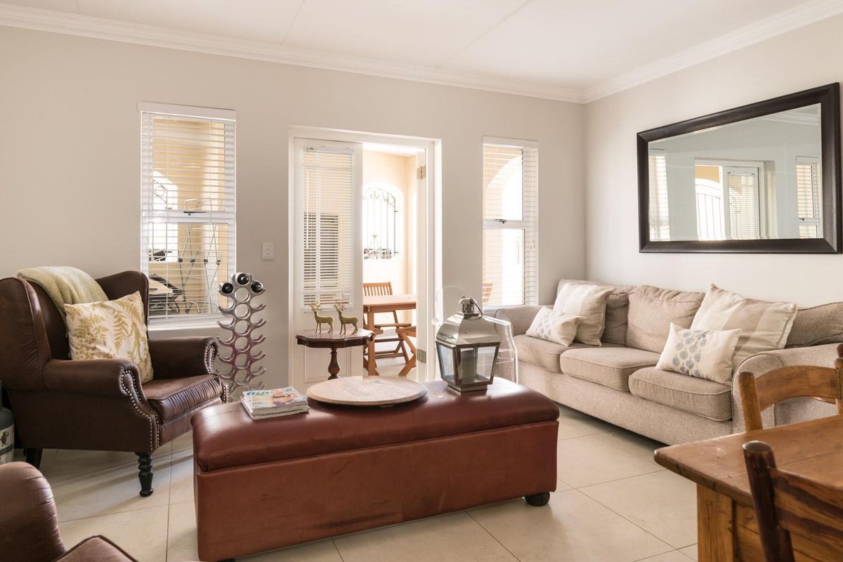 A bright and well-maintained living room featuring neutral tiled flooring, cove cornicing, and direct access to an outdoor patio area through a glass sliding door.