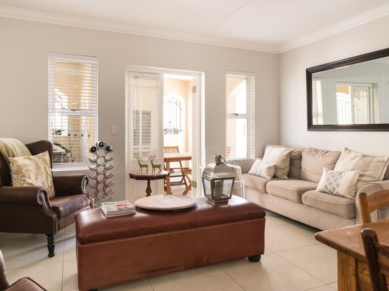 A bright and well-maintained living room featuring neutral tiled flooring, cove cornicing, and direct access to an outdoor patio area through a glass sliding door.