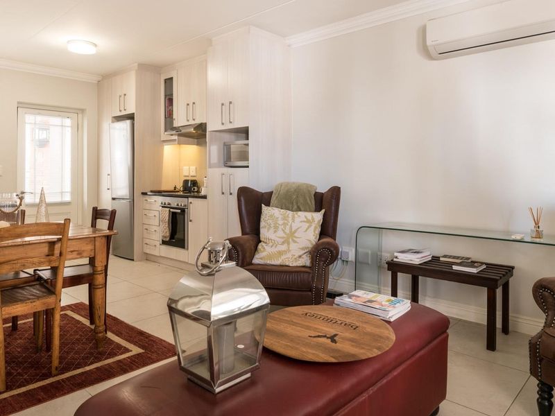 Open-plan living and dining area featuring a compact kitchen with built-in cabinetry, modern appliances, and a wall-mounted air conditioning unit.