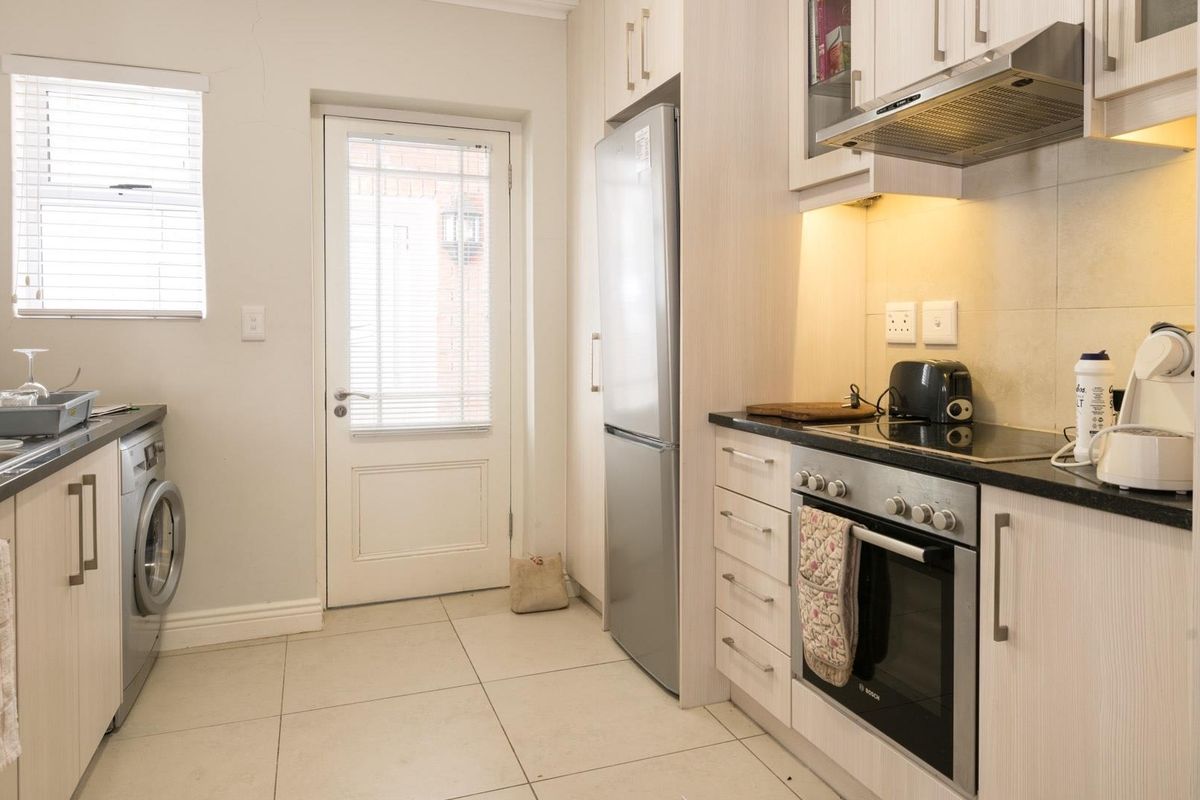 A functional kitchen featuring light wood-grain cabinetry, dark countertops, integrated oven and hob, and tiled flooring with direct access to an exterior door.