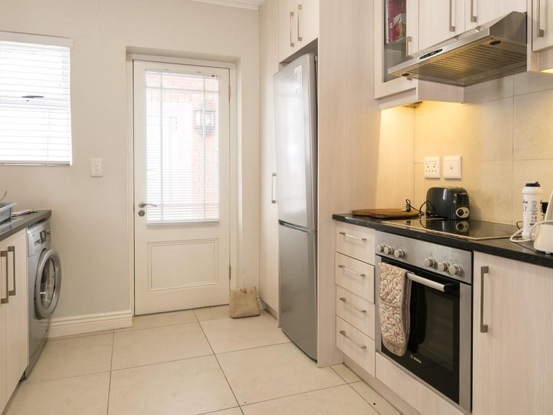A functional kitchen featuring light wood-grain cabinetry, dark countertops, integrated oven and hob, and tiled flooring with direct access to an exterior door.