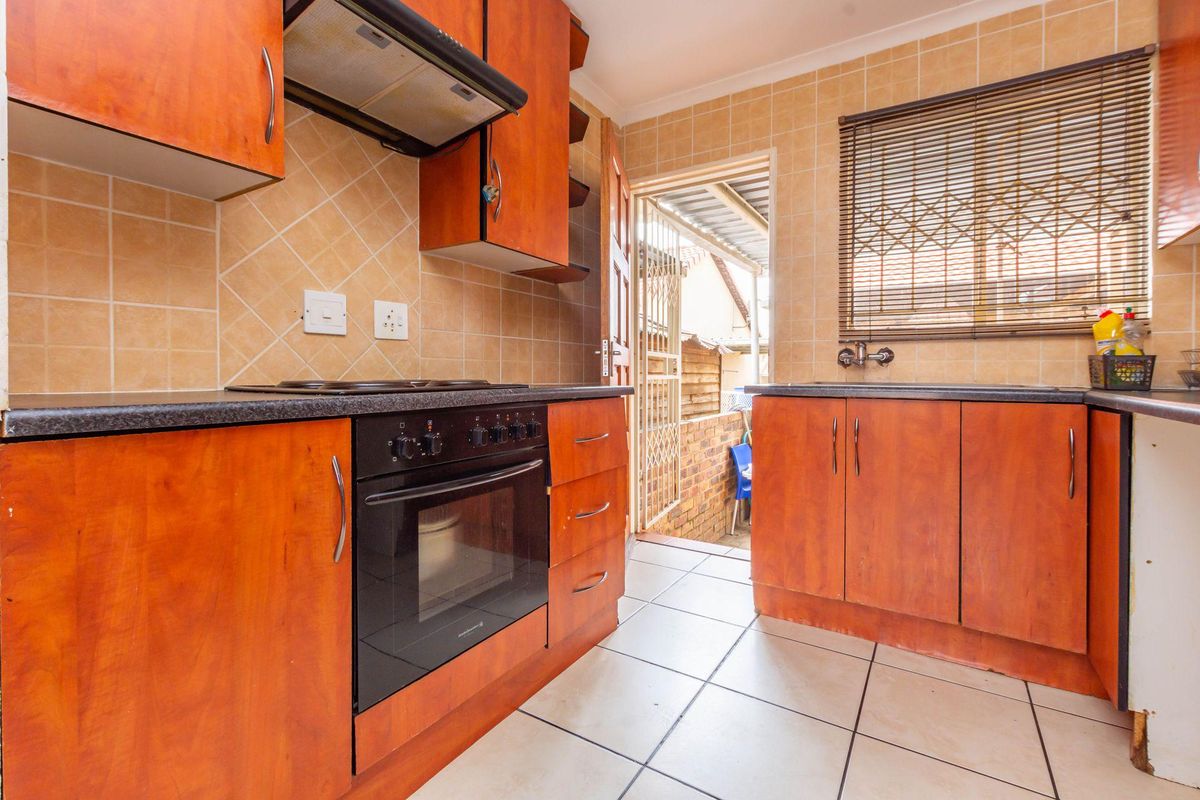 Functional kitchen featuring wood-look cabinetry, built-in oven, extractor fan, tiled splashbacks, and direct access to an outdoor area.