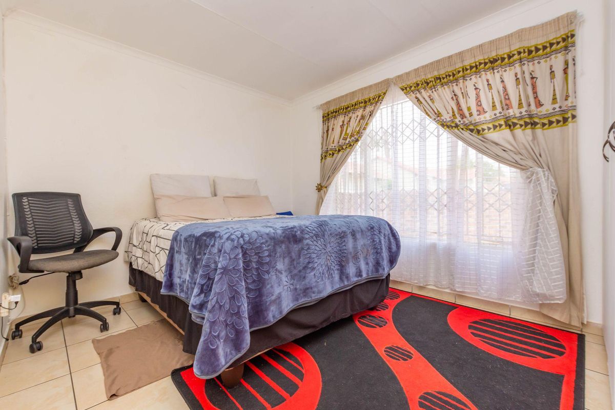 A bedroom featuring tiled flooring and a window fitted with security bars and curtains.