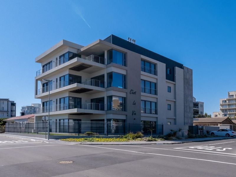 Modern multi-story apartment building featuring contemporary architectural design, large glass windows, and private balconies, situated on a corner lot.