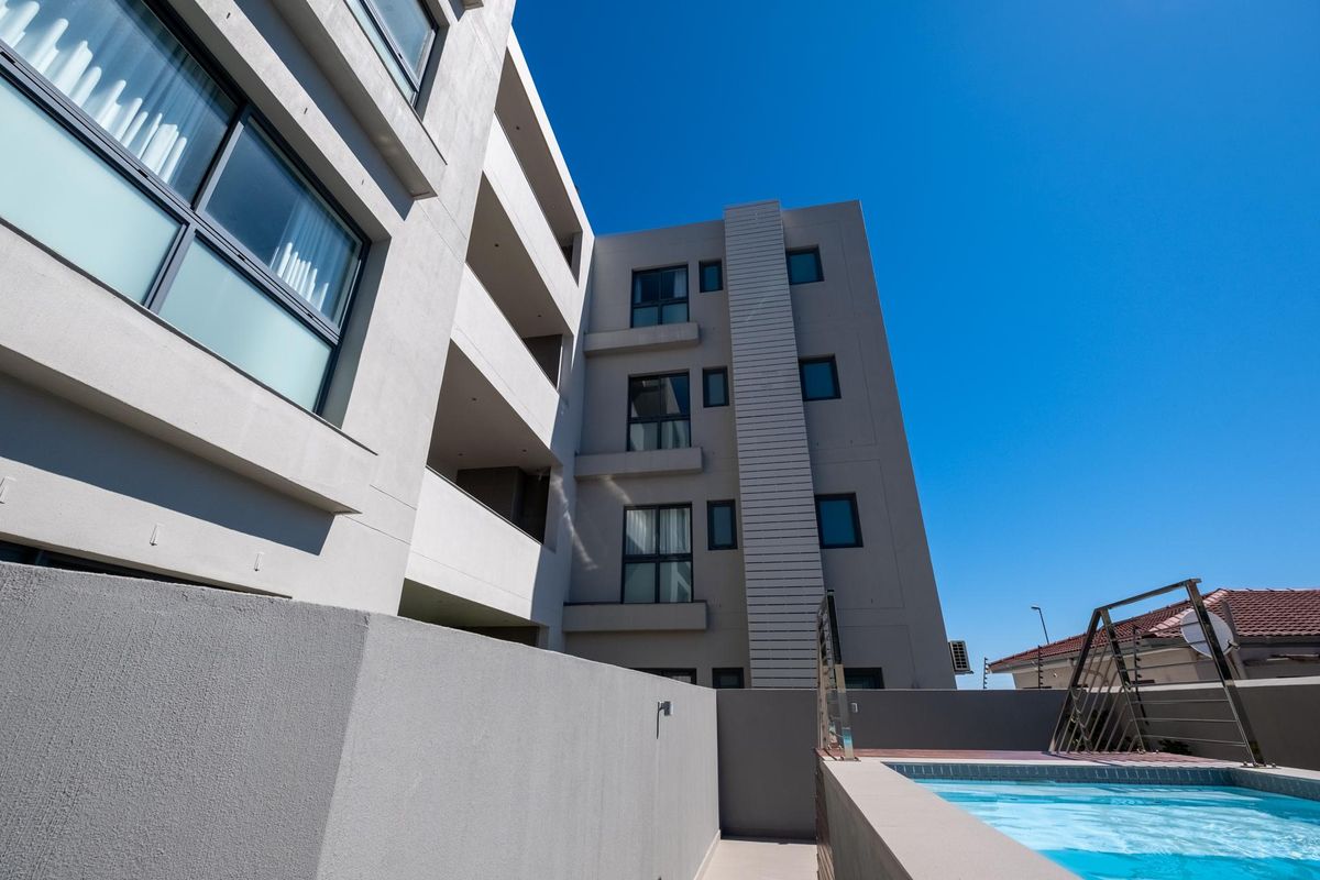 A modern multi-story residential building exterior featuring a swimming pool, clean architectural lines, and contemporary facade finishes.