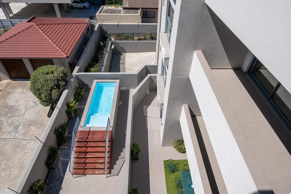 Aerial view of a modern property featuring a rectangular swimming pool, timber decking, tiled patio area, and perimeter boundary walls.