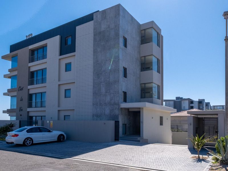 Modern multi-story residential building featuring contemporary architectural design, stone cladding, and paved driveway access.