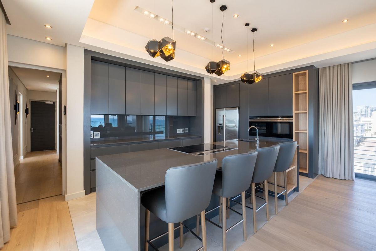 Modern open-plan kitchen featuring dark cabinetry, a large central island with integrated cooktop, stone countertops, and high-end built-in appliances.