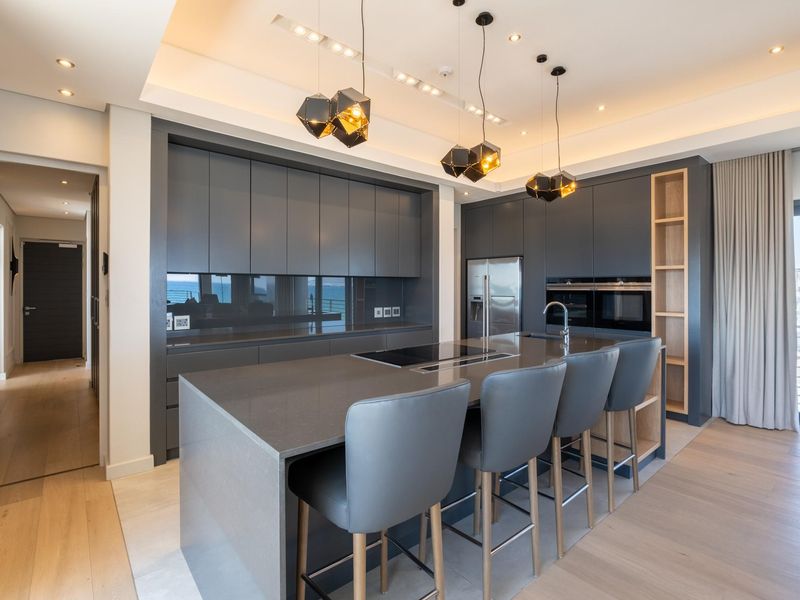 Modern open-plan kitchen featuring dark cabinetry, a large central island with integrated cooktop, stone countertops, and high-end built-in appliances.