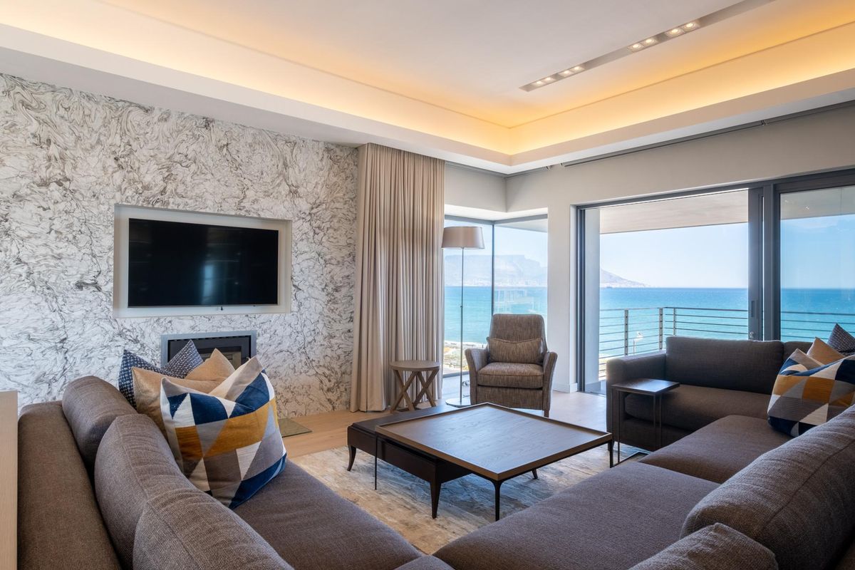 Modern living room featuring a striking marble feature wall, recessed ceiling lighting, and large sliding doors opening to a balcony with ocean views.