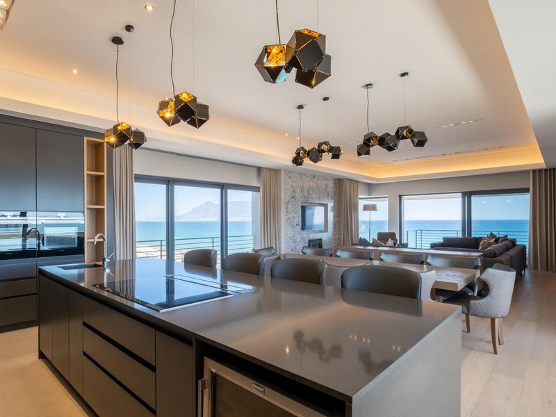 Modern open-plan kitchen and living area featuring a large island, integrated appliances, recessed lighting, and expansive sliding doors with panoramic ocean views.
