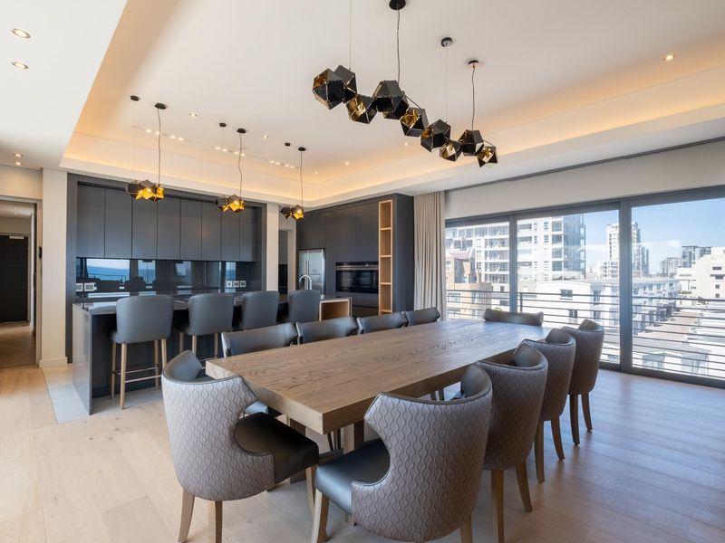 Modern open-plan kitchen and dining area featuring sleek dark cabinetry, integrated appliances, recessed ceiling lighting, and large sliding doors leading to a balcony.