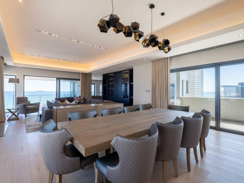 Spacious open-plan living and dining area featuring modern recessed lighting, contemporary pendant fixtures, light timber flooring, and large sliding glass doors leading to a balcony.