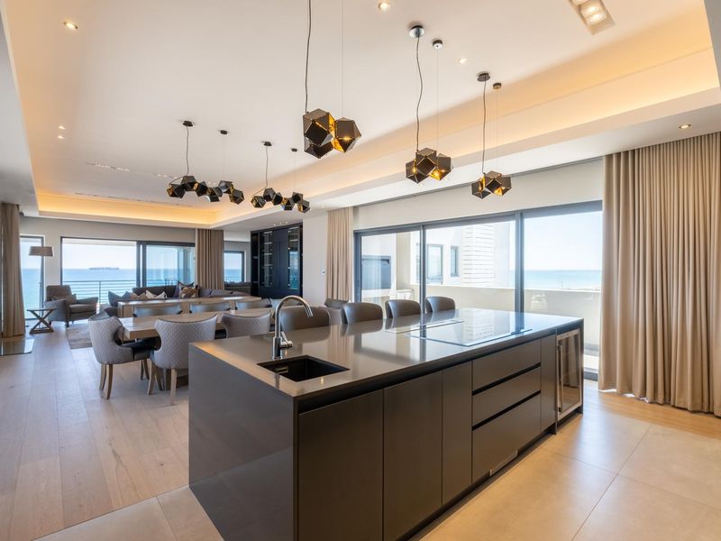 Modern open-plan living area featuring a sleek kitchen island with integrated sink and hob, flowing seamlessly into a spacious dining and lounge area.