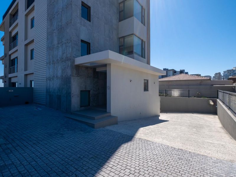 Modern multi-story residential building exterior featuring concrete facade, paved driveway, and covered entrance area.