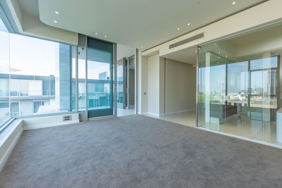 Spacious modern living area featuring floor-to-ceiling glass windows, recessed lighting, ducted air conditioning, and a glass-enclosed office space with neutral carpeting.