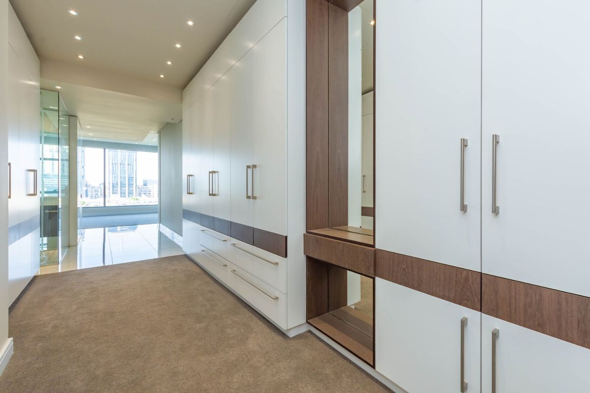 A spacious dressing area featuring extensive floor-to-ceiling built-in cabinetry with integrated shelving and mirror accents, finished with modern hardware.