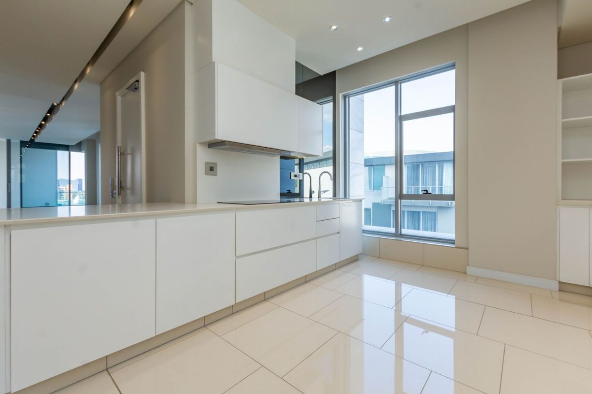 Modern kitchen featuring sleek white cabinetry, integrated appliances, polished tile flooring, and large windows providing ample natural light.