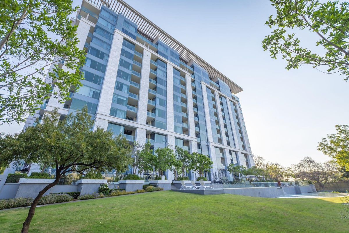 A low-angle exterior view of a modern high-rise apartment building featuring glass facades, stone cladding, and landscaped grounds with a pool area.