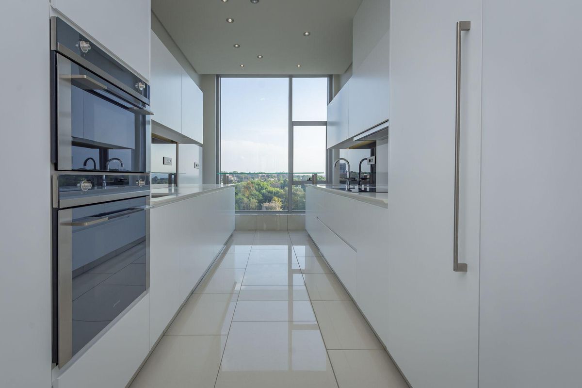 Modern galley-style kitchen featuring sleek white cabinetry, integrated appliances, polished tile flooring, and a large window offering expansive views.