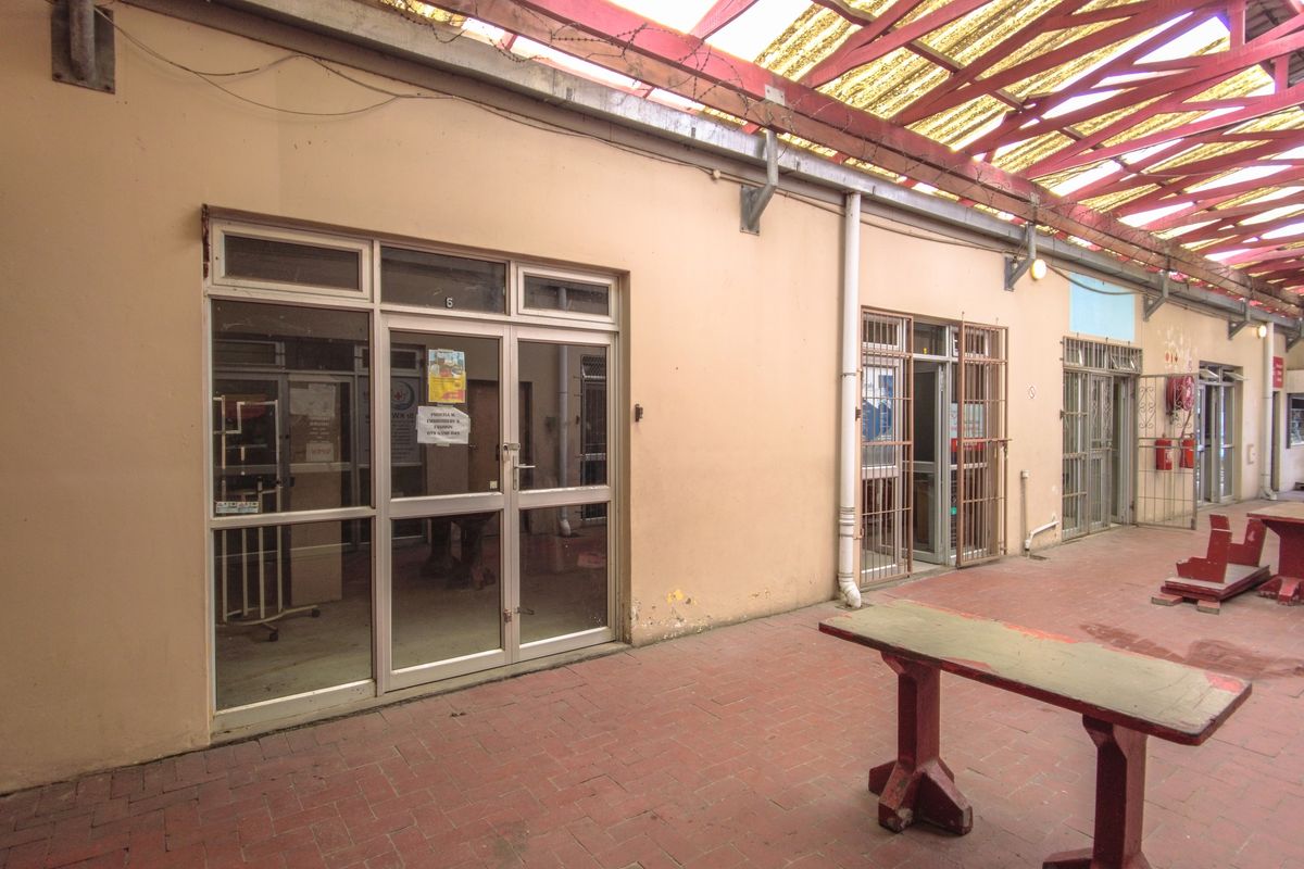 Exterior view of a retail unit featuring a covered walkway, brick paving, and multiple glass-paneled entrance doors with security gates.