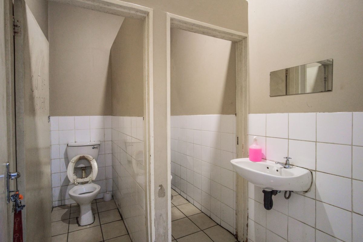A functional commercial restroom facility featuring two toilet cubicles and a wall-mounted basin with a mirror.