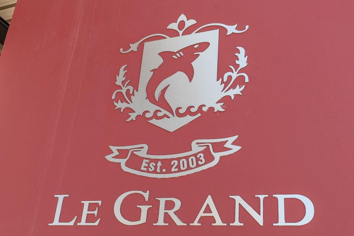 A close-up view of a sign displaying the name Le Grand and a shark emblem, established in 2003.