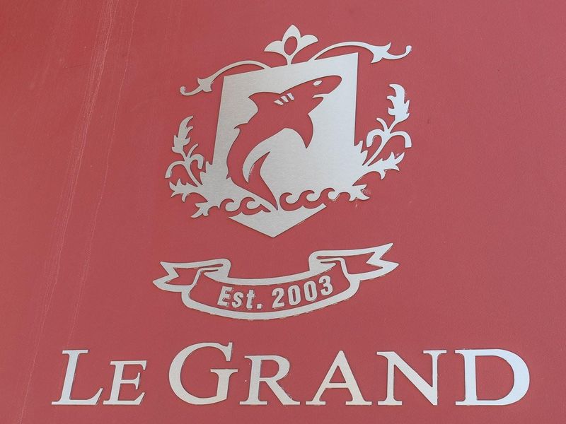 A close-up view of a sign displaying the name Le Grand and a shark emblem, established in 2003.