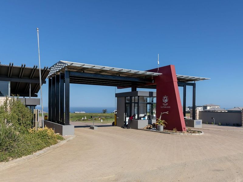 Modern security gatehouse entrance for the residential estate featuring paved driveway access, solar panel roofing, and contemporary architectural steel and stone finishes.