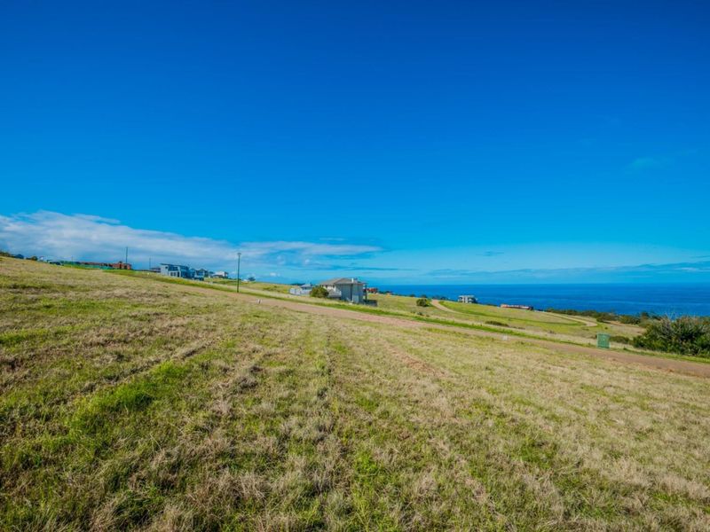A wide-angle view of a vacant residential plot featuring a gentle slope and expansive coastal ocean views.