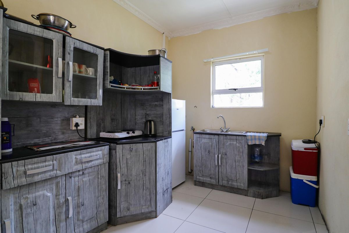 A functional kitchen featuring wood-grain cabinetry, a stainless steel sink, tiled flooring, and a window providing natural light.