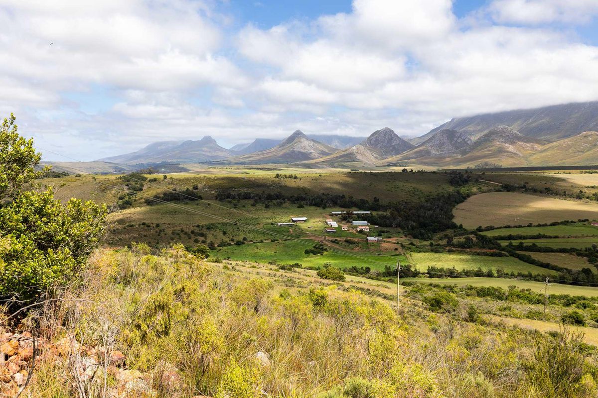 A wide-angle aerial view of a rural farm property nestled in a valley, surrounded by expansive green fields and dramatic mountain ranges.