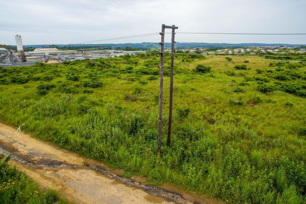 An aerial view of a vacant commercial land plot featuring natural vegetation, a dirt access path, and overhead utility poles.