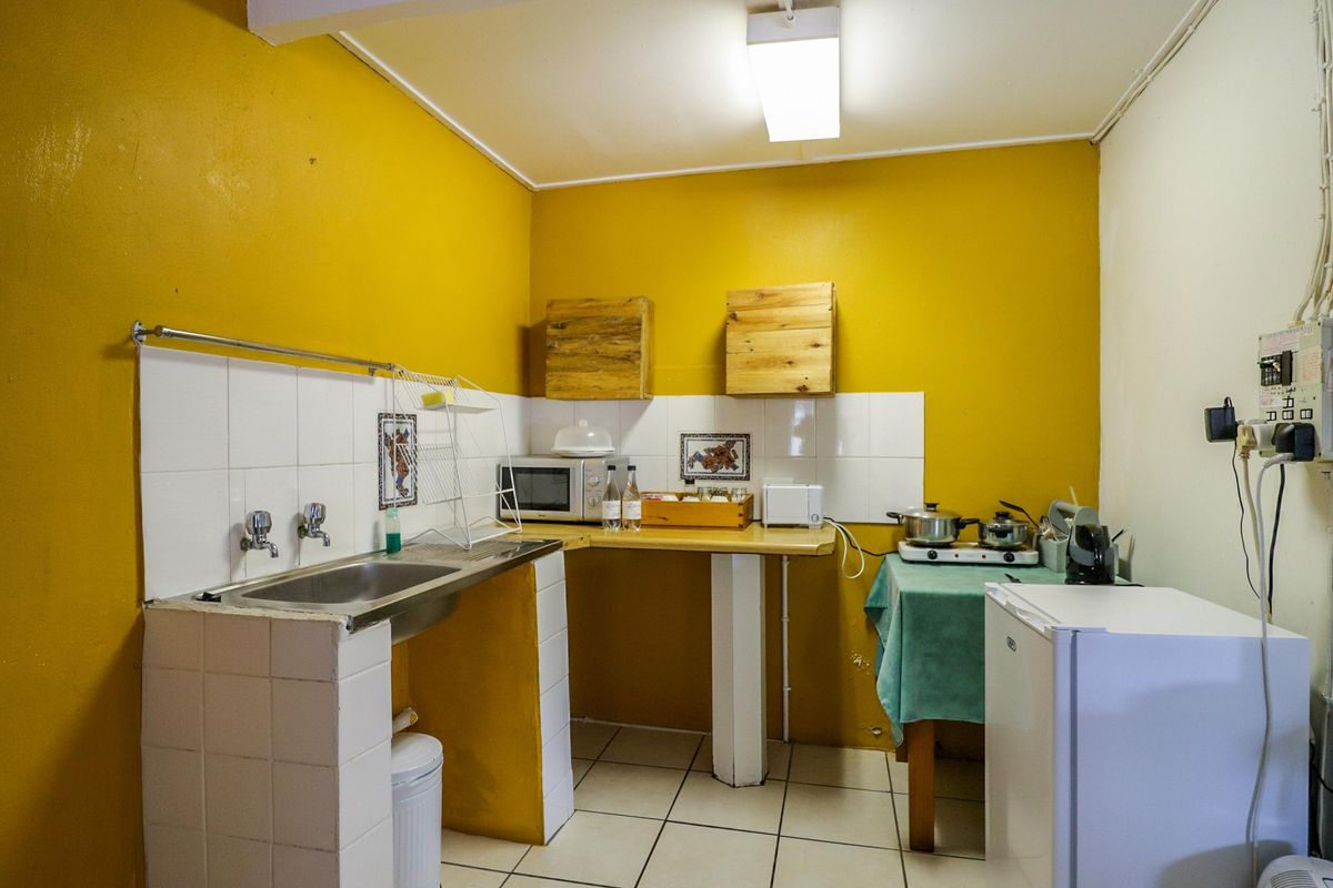 A compact kitchen area featuring tiled sink surround, basic cabinetry, and yellow painted walls, offering a functional space for food preparation.