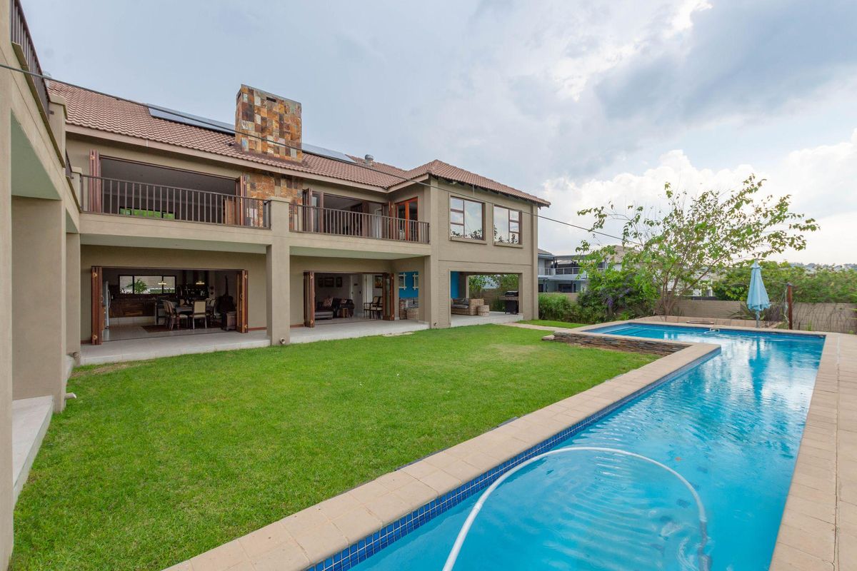 Spacious rear exterior view featuring a large swimming pool, manicured lawn, covered patio area, and a two-story residence with stone chimney detail.
