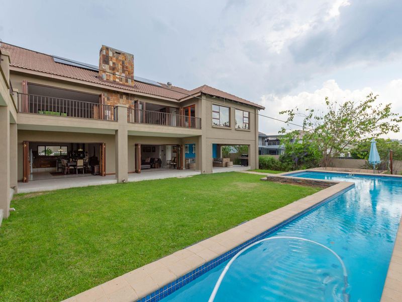 Spacious rear exterior view featuring a large swimming pool, manicured lawn, covered patio area, and a two-story residence with stone chimney detail.